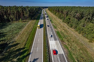 Aerial view of a multi-lane motorway with flowing traffic of cars and lorries running through a wooded landscape.
