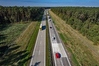 Aerial view of a multi-lane motorway with flowing traffic of cars and lorries running through a wooded landscape.