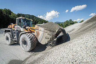 Radlader beim Verladen von Schotter vor großen Kieshalden im Diabaswerk Saalfelden