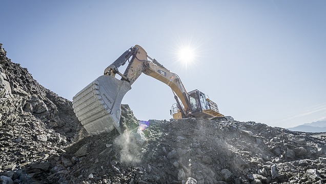 Hydraulikbagger bewegt und zerkleinert Gestein auf einer Halde mit losem Material unter freiem Himmel.