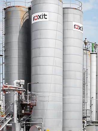 Several large, vertical bitumen storage tanks in an industrial plant, connected by pipework and ladders, as part of a comprehensive complete bitumen solution.