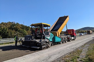 Straßenbaumaschine verarbeitet aufbereitete Asphaltmaterialien direkt auf der Fahrbahn, während ein Lkw das Material zuführt