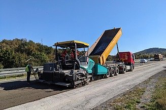 Straßenbaumaschine verarbeitet aufbereitete Asphaltmaterialien direkt auf der Fahrbahn, während ein Lkw das Material zuführt