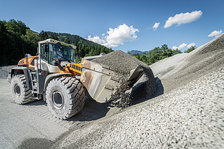Radlader beim Verladen von Schotter vor großen Kieshalden im Diabaswerk Saalfelden