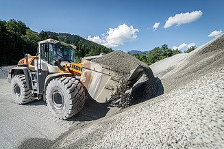 Radlader beim Verladen von Schotter vor großen Kieshalden im Diabaswerk Saalfelden