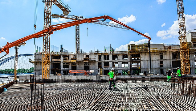 A building and civil engineering site with cranes, reinforcement and a concrete pump being used to pour concrete into a reinforced concrete structure
