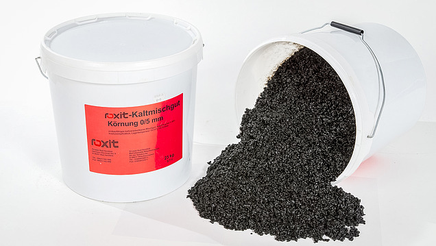 Bitumen-based cold mix in buckets, whereby the black asphalt mix is poured out of a plastic container.