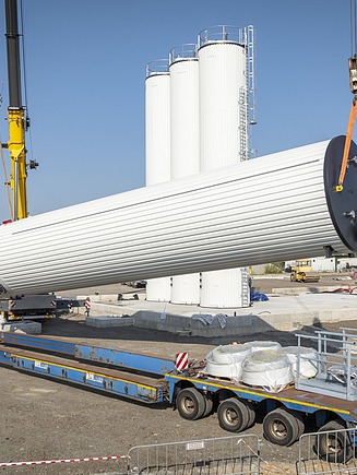 Assembly of a large-dimensioned bitumen tank on an industrial construction site, where a cylindrical steel container is installed using cranes.