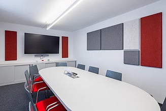 Meeting room with oval table, chairs and acoustic panels mounted on the walls in different colours and formats.