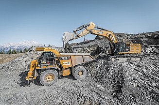 Hydraulikbagger lädt Gesteinsmaterial in einen Muldenkipper auf einer Halde mit losem Schüttgut in einem Abbau- oder Aufbereitungsbereich.