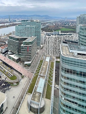 Aerial view of an urban building complex with several flat roofs, some of which are green, between modern office and residential buildings.