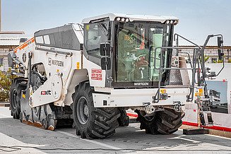 Straßenfräsmaschine von Wirtgen mit großen Rädern und Fräseinheit steht auf einem Betriebsgelände; sichtbar sind Fahrerkabine, Hydraulikkomponenten und Anbaugeräte – Teil des eigenen Maschinenparks für die Straßeninstandhaltung.