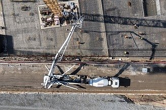 A concrete pump is delivering fresh concrete to a large, reinforced construction site, whilst several people are preparing to spread it over the steel reinforcement.