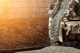 Fresh concrete flows out of a chute, revealing a mixture of cement paste and coarse aggregates as it spreads across a building site.