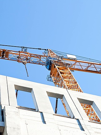 Turmdrehkran steht über einer Betonrohbaukonstruktion mit Öffnungen im Gebäude, vor einem klaren blauen Himmel aufgenommen.