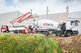 A concrete mixer and concrete pump in action on a building site in front of a concrete wall; the concrete is being processed on site