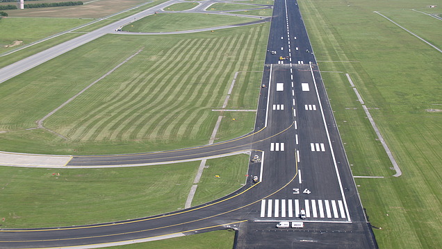 Luftaufnahme einer Flughafen‑Start‑ und Landebahn mit Taxiways, Markierungen und umliegenden Infrastrukturflächen