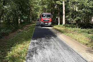 Road surface is treated with bitumen emulsion while a lorry is in operation on a narrow road in the forest