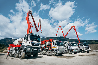 Several concrete pump trucks with their booms extended are standing by on a building site