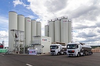 Moderne roxit PmB-Anlage am Standort Planá mit mehreren Silotürmen und zwei Tanklastwagen auf dem Betriebsgelände unter bewölktem Himmel.