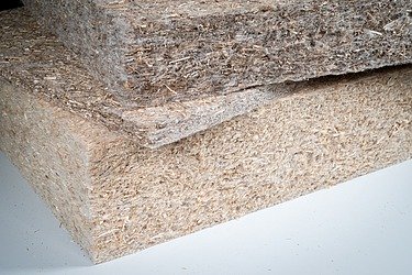 Gestapelte Bauplatten aus Naturfasern mit sichtbarer faseriger Struktur, dargestellt als nachhaltiges Baumaterial auf neutralem Untergrund.