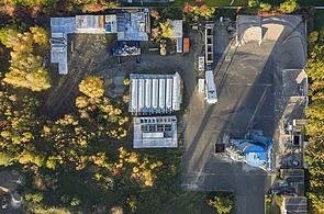 Aerial view of a concrete mixing plant under construction with silos, plant technology, storage areas and access roads, surrounded by vegetation; the construction and erection of a mobile concrete mixing plant for concrete production on a construction site is shown.