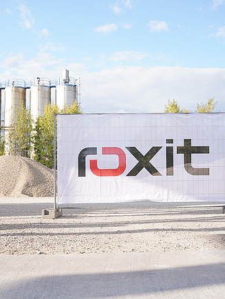 Company sign of roxit in front of a modern production plant with gravel pile - 