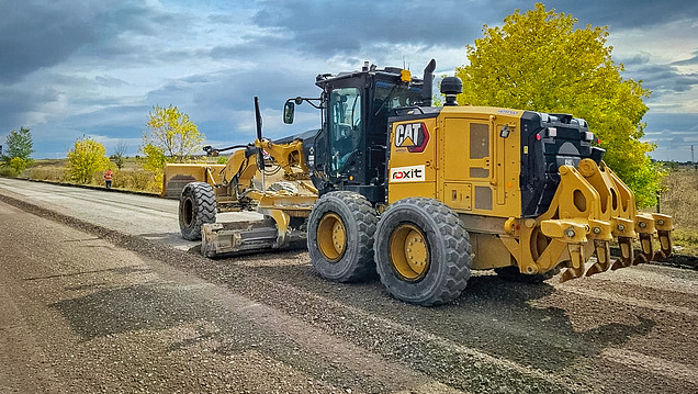 A road-construction machine (grader) is levelling an unpaved road on a construction site in open countryside