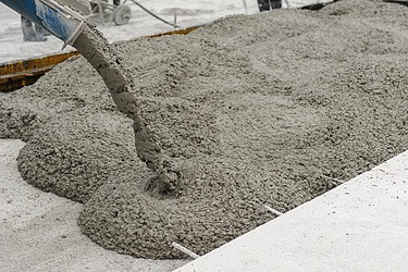 Fresh concrete is poured from a delivery hose line into a mould and spread over the prepared surface.