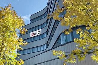 Modern office façade with roxit logo, surrounded by autumnal trees under a blue sky