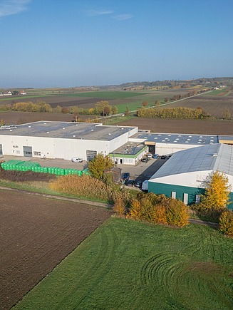 Aerial view of a production and storage site in a rural setting with several hall buildings, outdoor storage areas and surrounding fields.