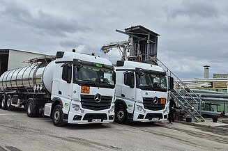 Zwei Tanklastwagen für den Bitumentransport stehen an einer industriellen Verladeanlage mit Rohrleitungen und Befülltechnik bereit.