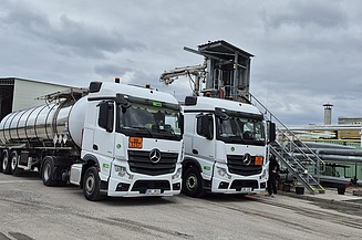 Two tanker lorries for bitumen transport are waiting at an industrial loading facility with pipelines and filling technology.