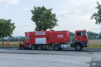 Multimac special vehicle with bitumen emulsion in use on a road; several people carrying out maintenance work