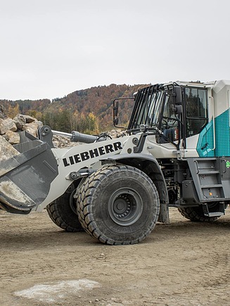 Wheel loader with H₂ labelling moves rock in a quarry; rock faces and stored material are visible in the background.