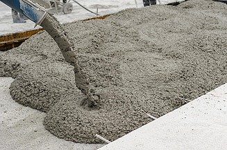 Fresh concrete is poured into the formwork through a delivery hose and spreads across the prepared surface.