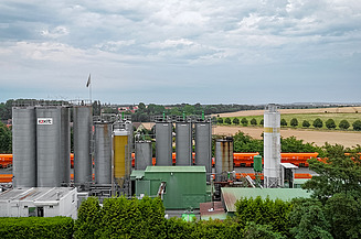 Industrial bitumen storage facility with several large storage tanks and connected rail transport, embedded in a rural environment.