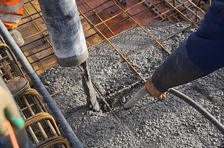 Fresh concrete is poured into reinforced formwork via a hose and compacted at the same time using an internal vibrator.
