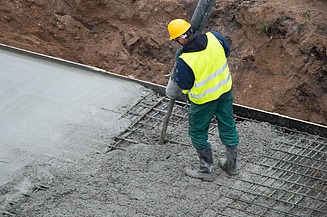 Person verdichtet frischen Beton mit einem Innenrüttler in einer Schalung mit Bewehrung, während sich die Oberfläche glättet und verdichtet.