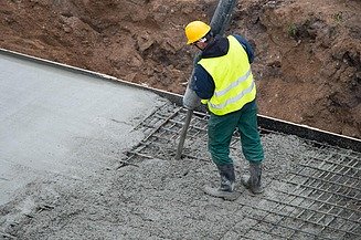A person is compacting fresh concrete using an internal vibrator inside a formwork containing reinforcement, whilst the surface is being smoothed and compacted.