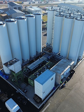 Aerial view of an industrial bitumen plant with several high storage tanks, connected pipelines and technical infrastructure on a factory site.