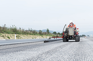 Use of bitumen emulsions in road construction: A sprayer applies bitumen along an asphalt edge on a construction site; the application is visible during infrastructure work on a prepared road surface.