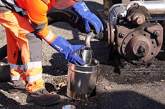 Specialised personnel remove bitumen emulsion from a technical plant for quality control and further processing in road construction.