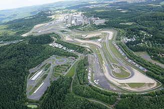 Aerial view of the Nürburgring with winding race track, grandstands and surrounding landscape