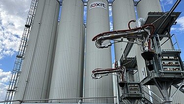 Moderne Siloanlagen und Anlagentechnik für polymermodifizierte Bitumen am roxit Standort Planá vor blauem Himmel mit Wolken.