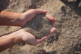 A close-up of two hands holding coarse sand and small pebbles.