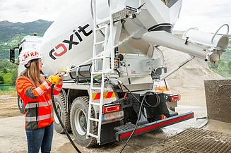 A concrete mixer is unloading concrete via a discharge chute at a construction site, whilst the machine is being cleaned with a water hose
